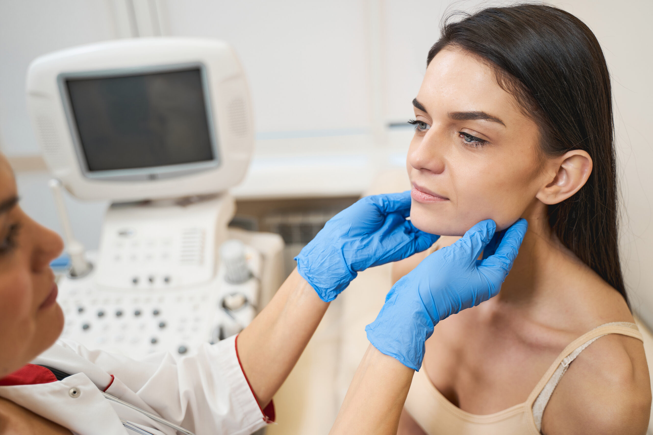 Professional medical worker standing in front of her patient while doing thyroid glands checkup